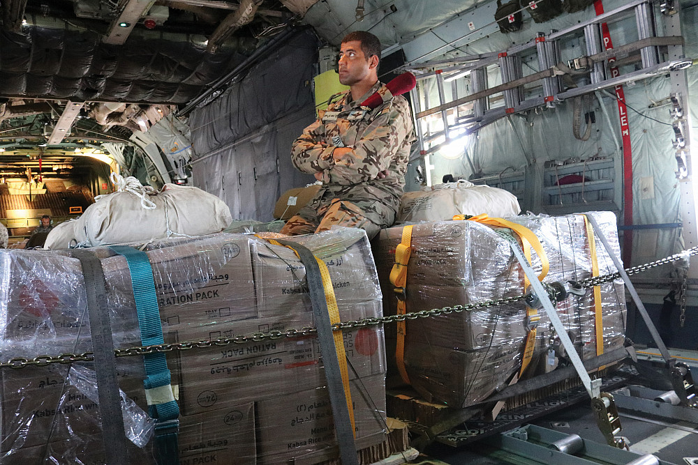 A man sits on food supplies in a C-130.