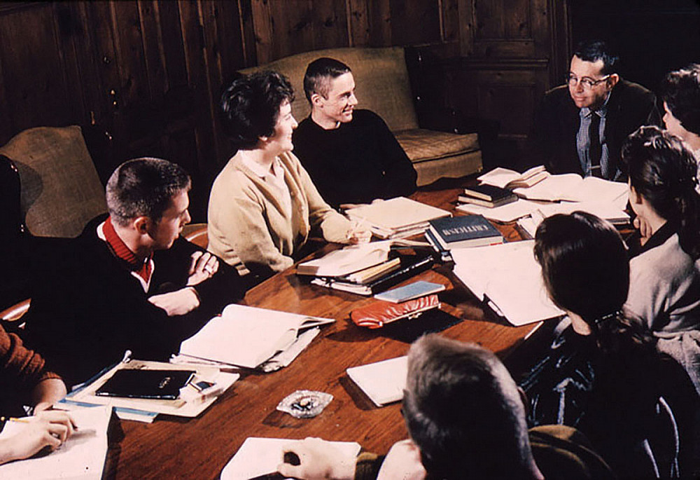 English professor David Stocking and students engage in explication around a seminar table in the 1960s, equipped with books, papers, and...