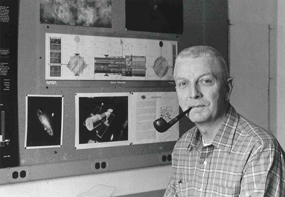 Daniel J. Schroeder ’55 with his pipe in front of schematics and images of Hubble.