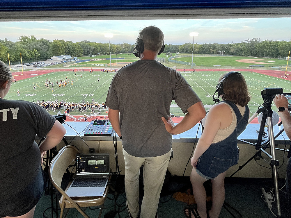 Matt Laszlo'92 and Meg Kulikowski'21 watching the 2024 Homecoming game from the announcers box.