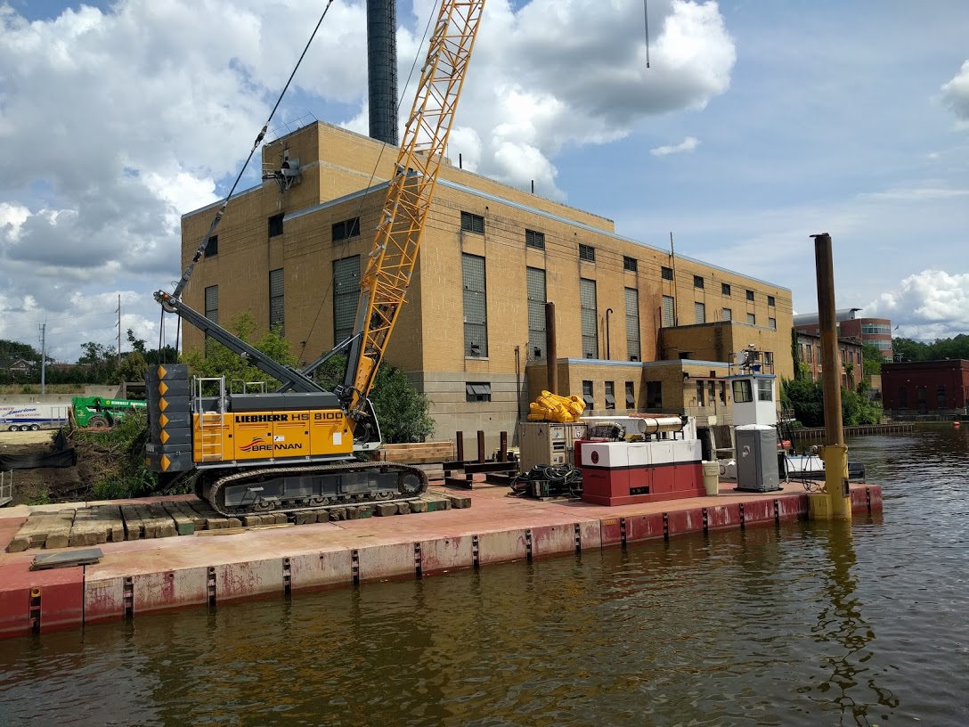 A crane floats on a barge on the Rock River next to the Powerhouse.